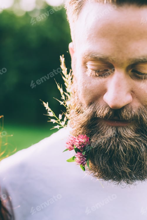 Preview: Close up on beard of young man adorned with pink flowers