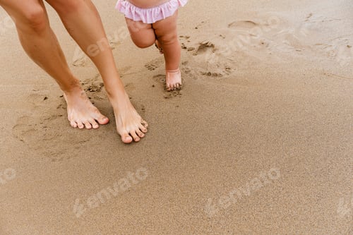 Preview: Baby's first steps. Mother and small child walking barefoot on beach sand near by ocean.