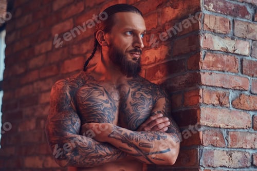 Preview: Handsome tattooed man with a stylish haircut and beard standing against a brick wall
