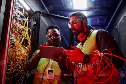 Preview: Two technicians using digital tablet setting up data network in neon light