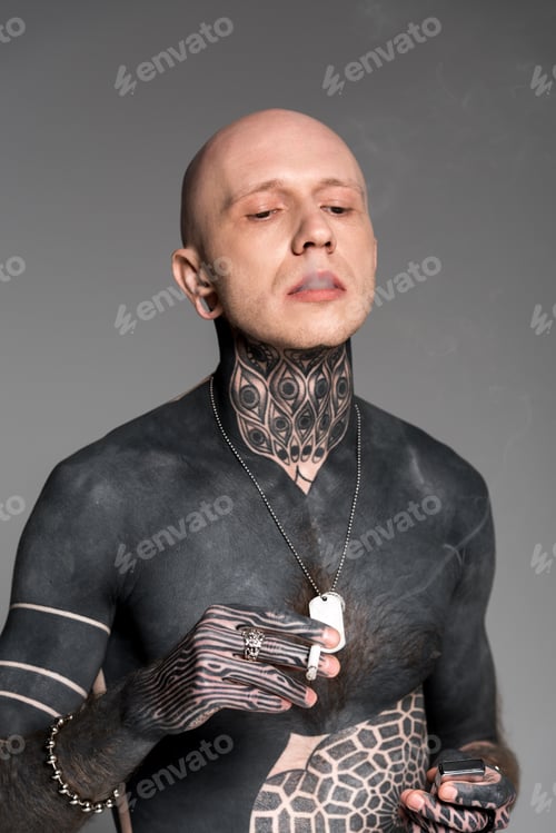 Preview: bald shirtless tattooed man holding lighter and smoking cigarette isolated on grey