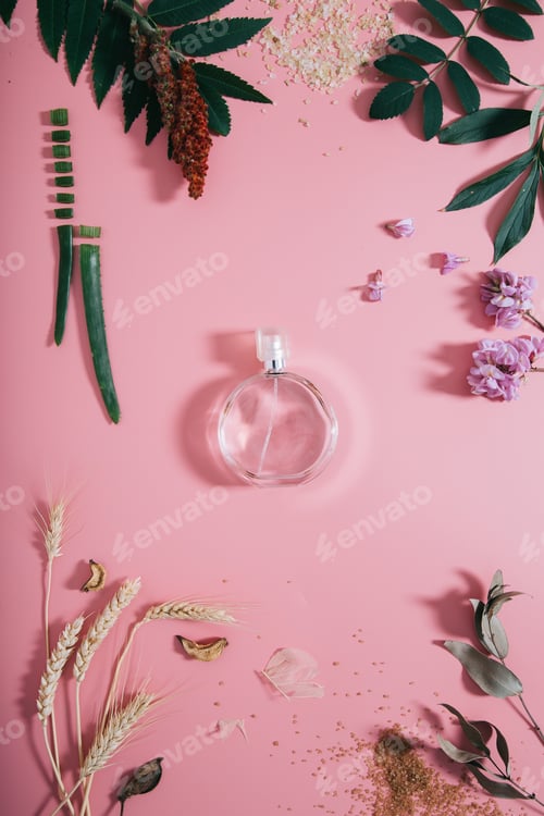 Vista previa: Transparent perfume bottle in flowers on pink background.