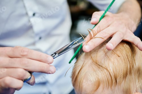 Preview: Behind shoulder view of male barber cutting little boy's hair.