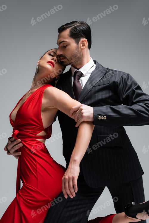 Preview: Low angle view of elegant man dancing tango with partner isolated on grey