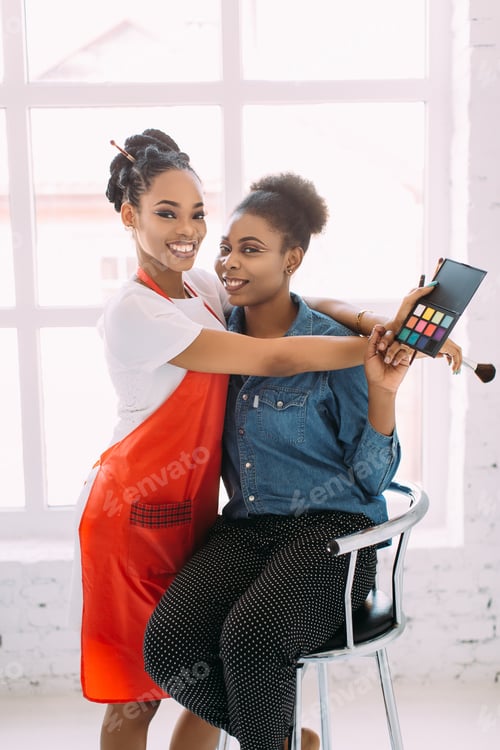 Preview: Young beautiful African American woman applying professional make-up by African make-up artist