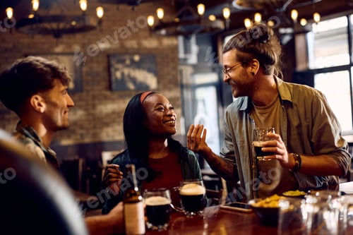 Preview: Happy black woman and her friend talking and drinking beer in a pub.