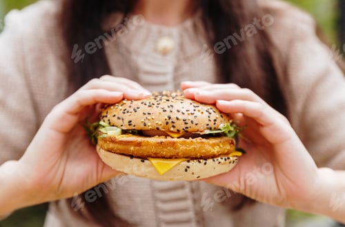 Preview: A young girl holds a delicious burger with both hands.