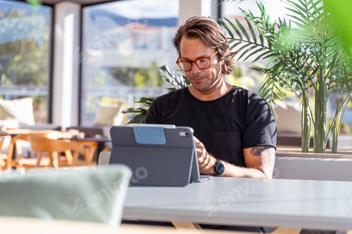 Preview: A man is sitting at a table working with his tablet and looking serious and concentrated