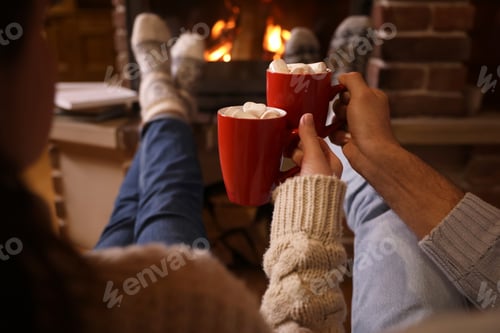 Preview: Couple with cups of delicious cocoa resting near fireplace at home, closeup. Winter vacation