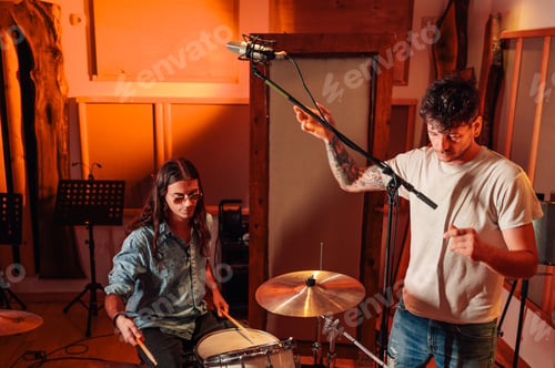 Preview: Drummer with assistant sound engineer setting up recording microphone in studio.