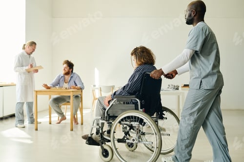 Preview: Young African American man in uniform pushing wheelchair with patient