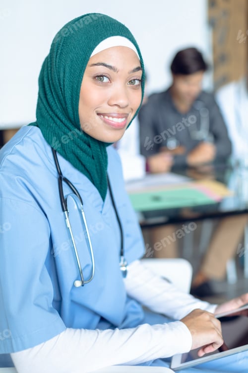 Preview: Happy surgeon female in hijab looking at camera while using digital tablet in the hospital