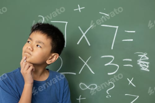 Preview: Schoolboy doing math on green chalkboard in a classroom at elementary school