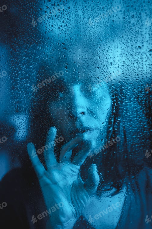 Preview: Woman looking out the window on a rainy day during the quarantine
