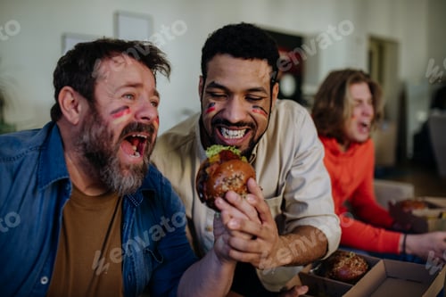 Preview: Happy German football fans friends watching football at home and eating hamburger.