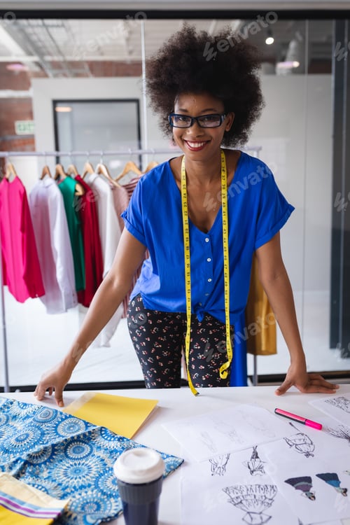 Preview: Happy mixed race fashion designer working in office with tailor centimeter on neck