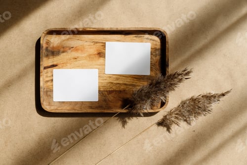 Preview: Top view of two blank paper sheet cards on a wooden tray with dry grass. Beige or sand tones