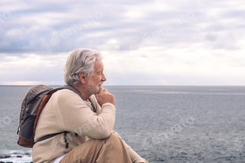 Preview: Adult senior man sitting on the cliff in sea excursion looking at horizon over water.