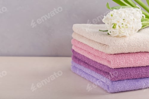 Preview: Stack of colorful bath towels with hyacinth flower on light background.