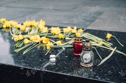 Preview: Red memorial candle and yellow daffodils on stone surface, commemorating the Warsaw Ghetto Uprising