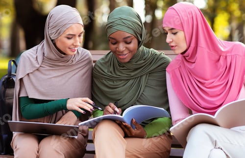 Preview: Three Female Arab Students Learning Together Reading Books Sitting Outdoors