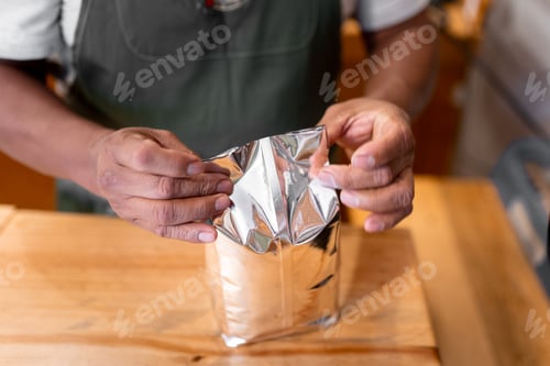 Preview: An Hispanic man is closing a bag full of ground coffee.