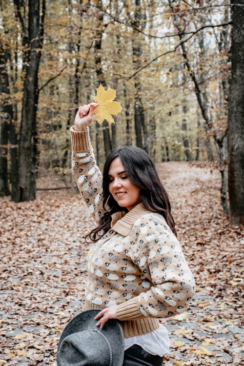 Preview: Shot of a beautiful woman in an autumn forest with a maple leaf on the hand