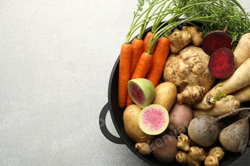 Preview: Different root vegetables in pot on light grey table, top view. Space for text