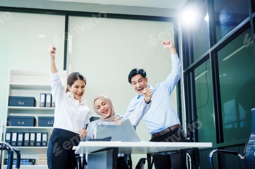 Preview: A Muslim businesswoman and an Asian woman sit with a middle-aged businessman at a desk a laptop