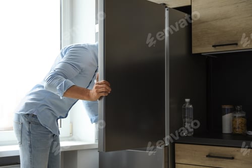 Preview: Man looking into refrigerator full of products in kitchen
