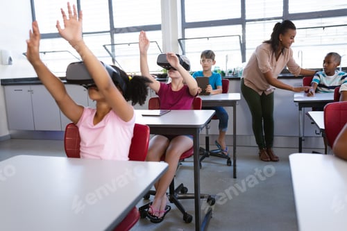 Preview: Group of diverse students using electronic devices while sitting on their desk in class at school
