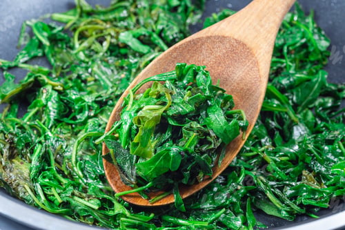 Preview: Preparing a side dish to steak, Wilted arugula or rocket salad in frying pan, horizontal, closeup