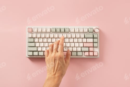 Preview: Female hand typing on keyboard on pink background. View from above. Flat lay.