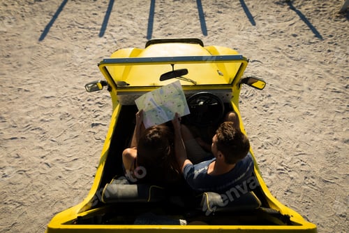 Preview: Happy caucasian couple sitting in beach buggy by the sea reading roadmap