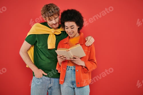 Preview: interracial couple hugging and reading book on coral background, cultural diversity, vibrant colors,