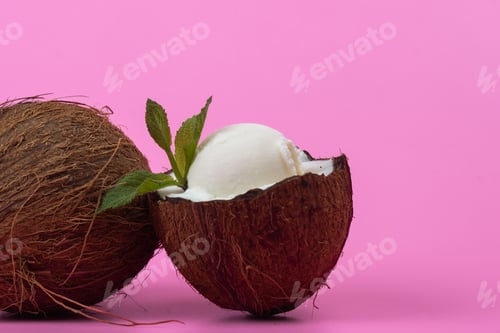Preview: Vanilla ice cream balls in fresh coconut halves decorated with mint leaves on a pink background