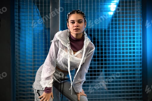 Preview: Young woman posing and looking at camera with background of wire and blue light