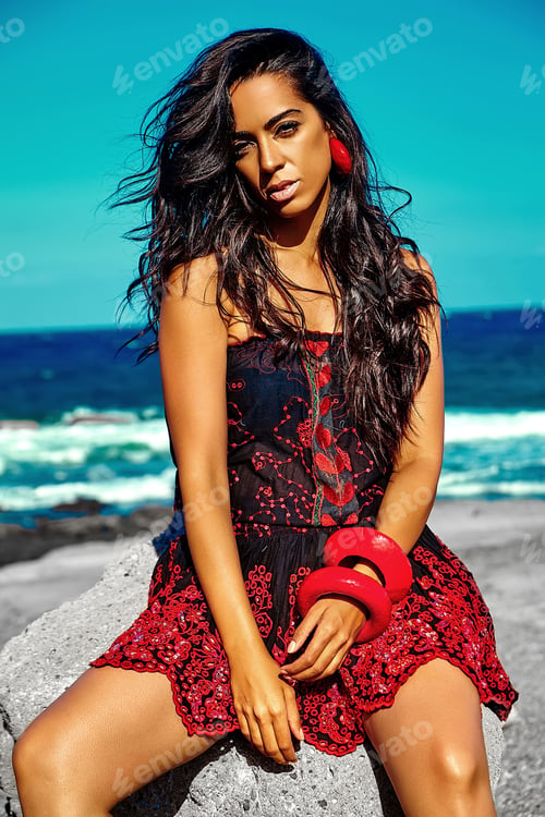 Preview: model girl in red colorful red dress posing behind blue beach ocean