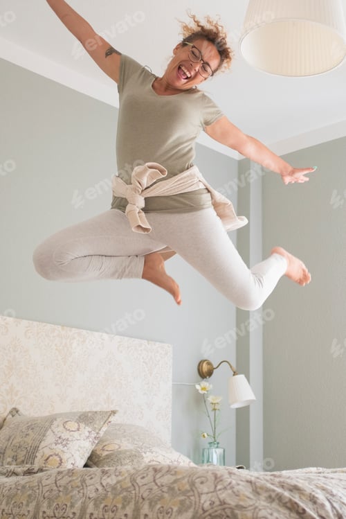 Preview: Young adult pretty woman go crazy for happiness and jump on the bed with coffee cup - overjoyed