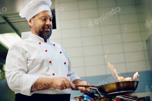 Preview: Mature chef preparing food in frying pan in a restaurant kitchen.