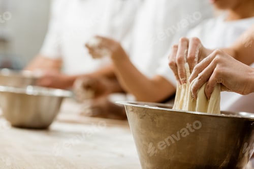 Preview: cropped shot of baking manufacture workers kneading dough together
