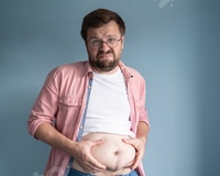 Vorschau: Unglücklicher, unzufriedener übergewichtiger Mann, hob T-Shirt und hält überschüssiges Bauchfett mit den Händen