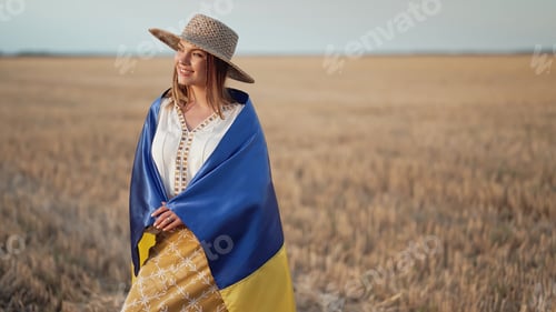 Preview: Smiling ukrainian woman with national flag in wheat field after harvesting.