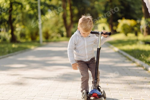 Preview: Little child learning to ride a scooter outdoors
