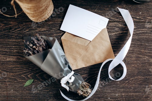 Preview: A little bouquet of flowers packed in dark paper, postcard, envelope and white ribbon are on the