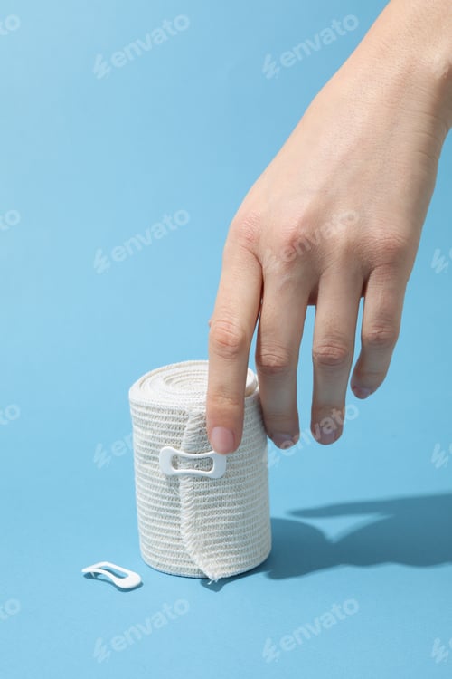 Preview: Concept of help during an injury, female hand and elastic bandage on blue background
