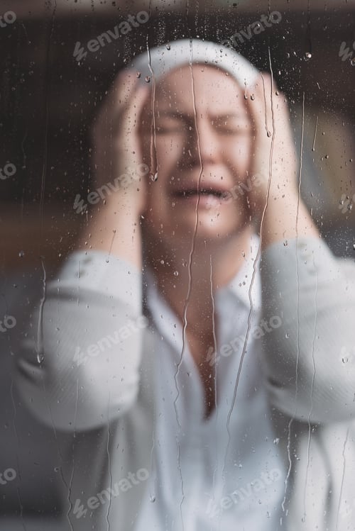 Preview: sick mature woman in kerchief crying behind window with raindrops