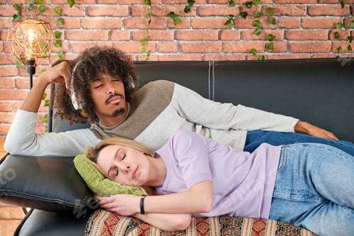 Preview: multiracial young couple lying on the sofa at home resting sleeping and listening to music