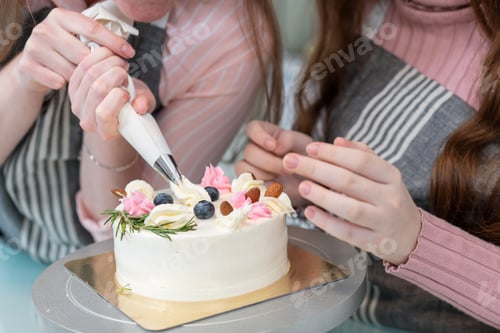 Preview: Hand of mother and daughter decorating topping on cake