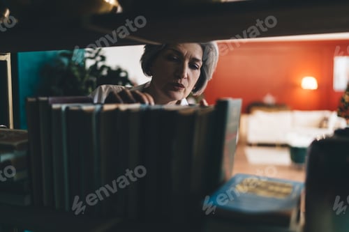 Preview: Focused mature woman searching books row in shelf